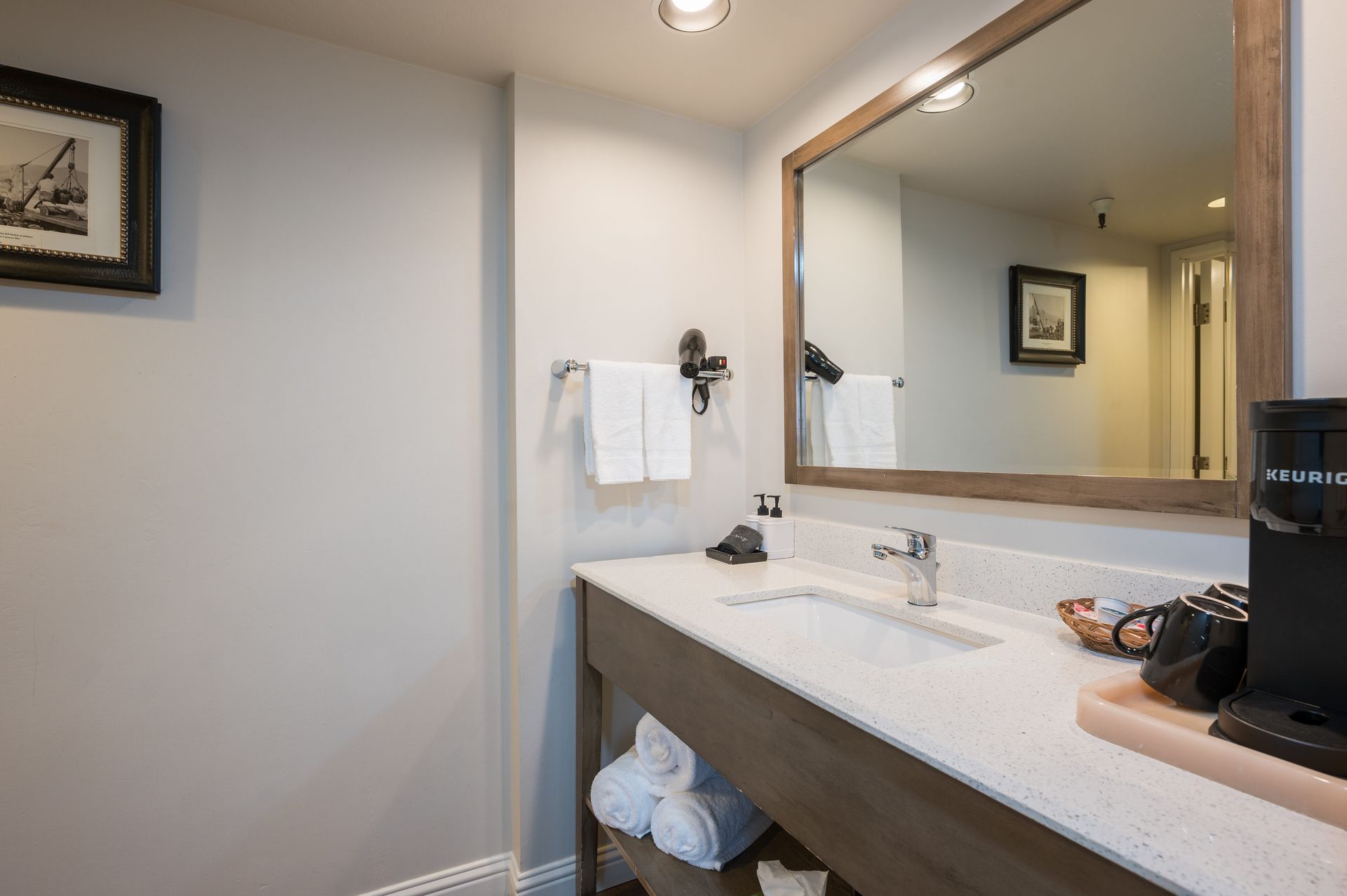 A bathroom in a hotel room with a sink , mirror and coffee maker.