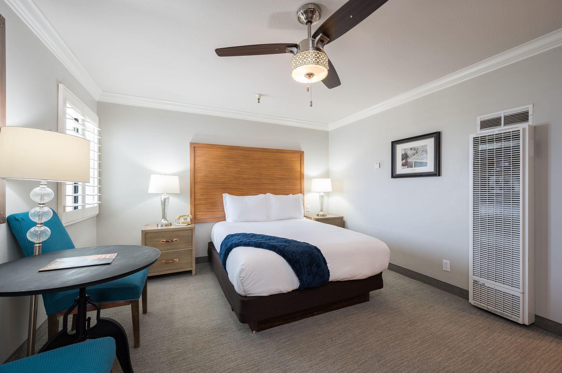 A hotel room with a king size bed , a table , chairs and a ceiling fan.