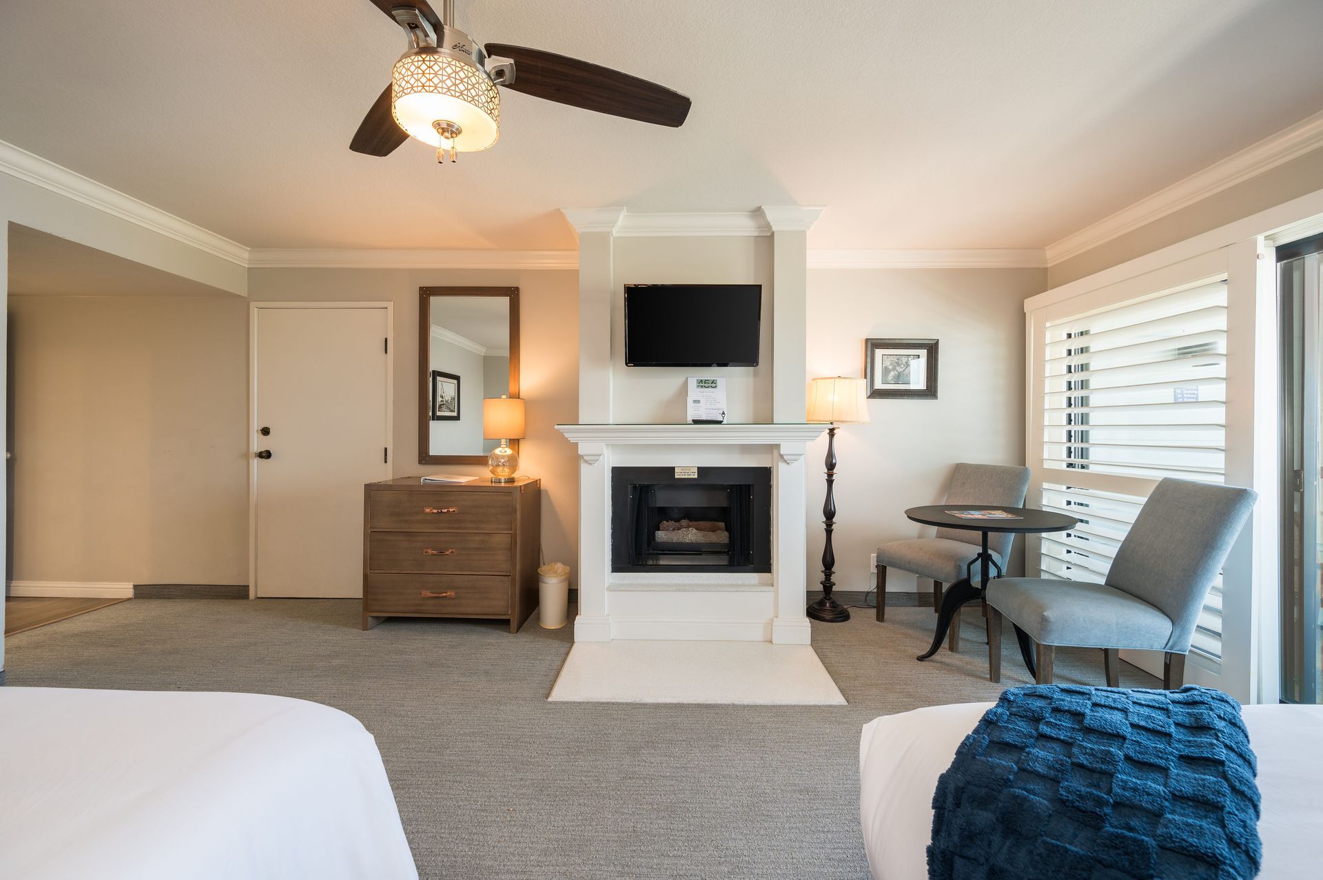 A hotel room with two beds , a fireplace , a television and a ceiling fan.