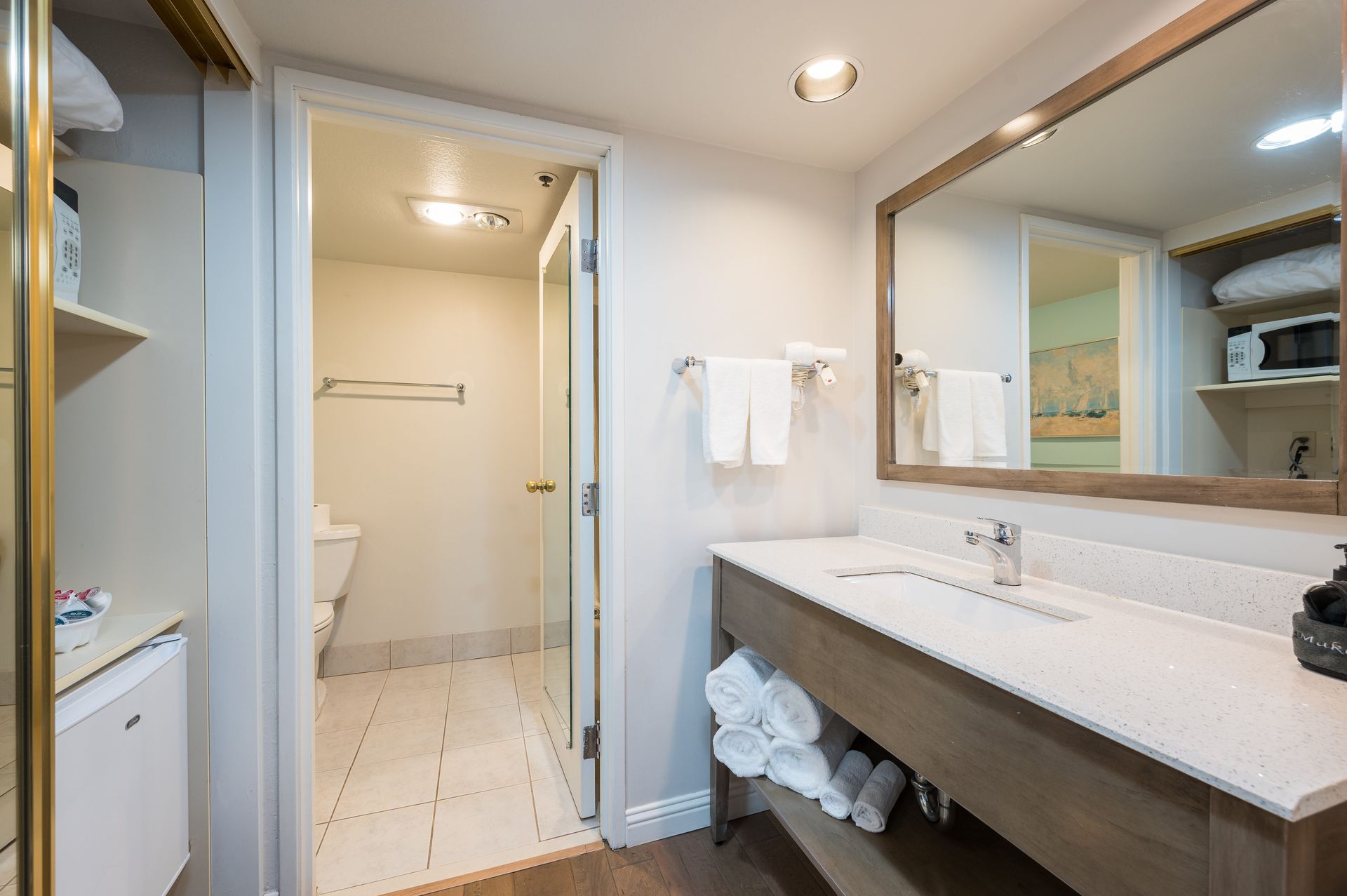 A bathroom in a hotel room with a sink , mirror and toilet.