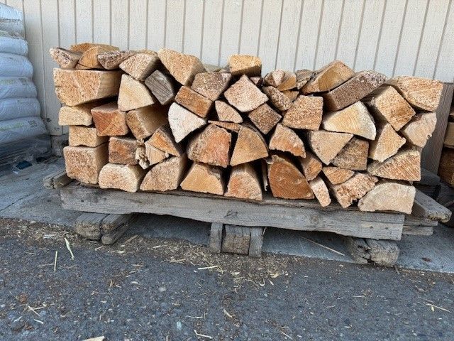 A pile of logs stacked on top of each other in front of a stone wall.