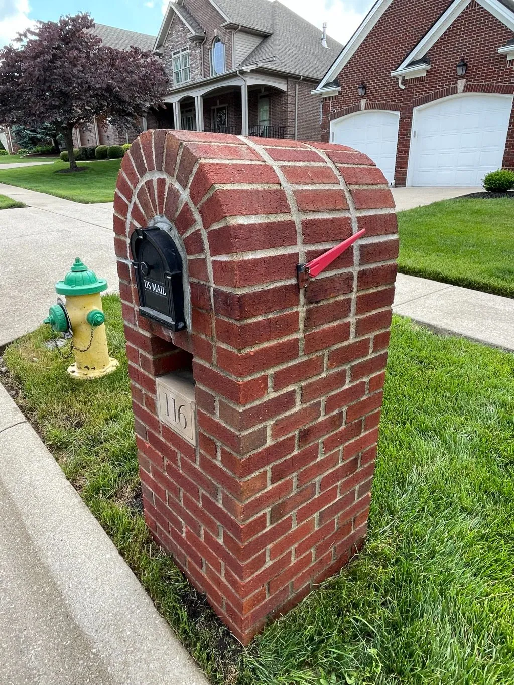 A red brick mailbox is sitting in the grass next to a fire hydrant.