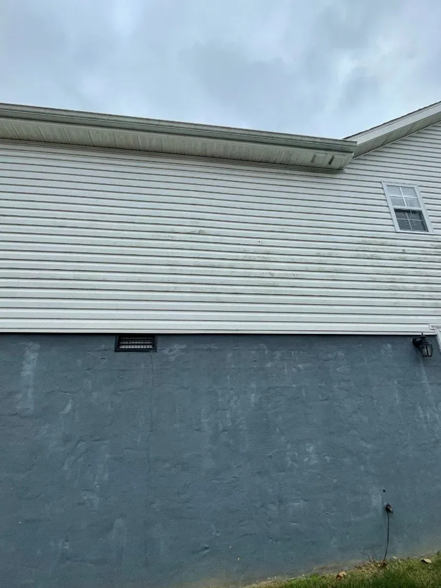 The side of a house with white siding and a blue foundation.
