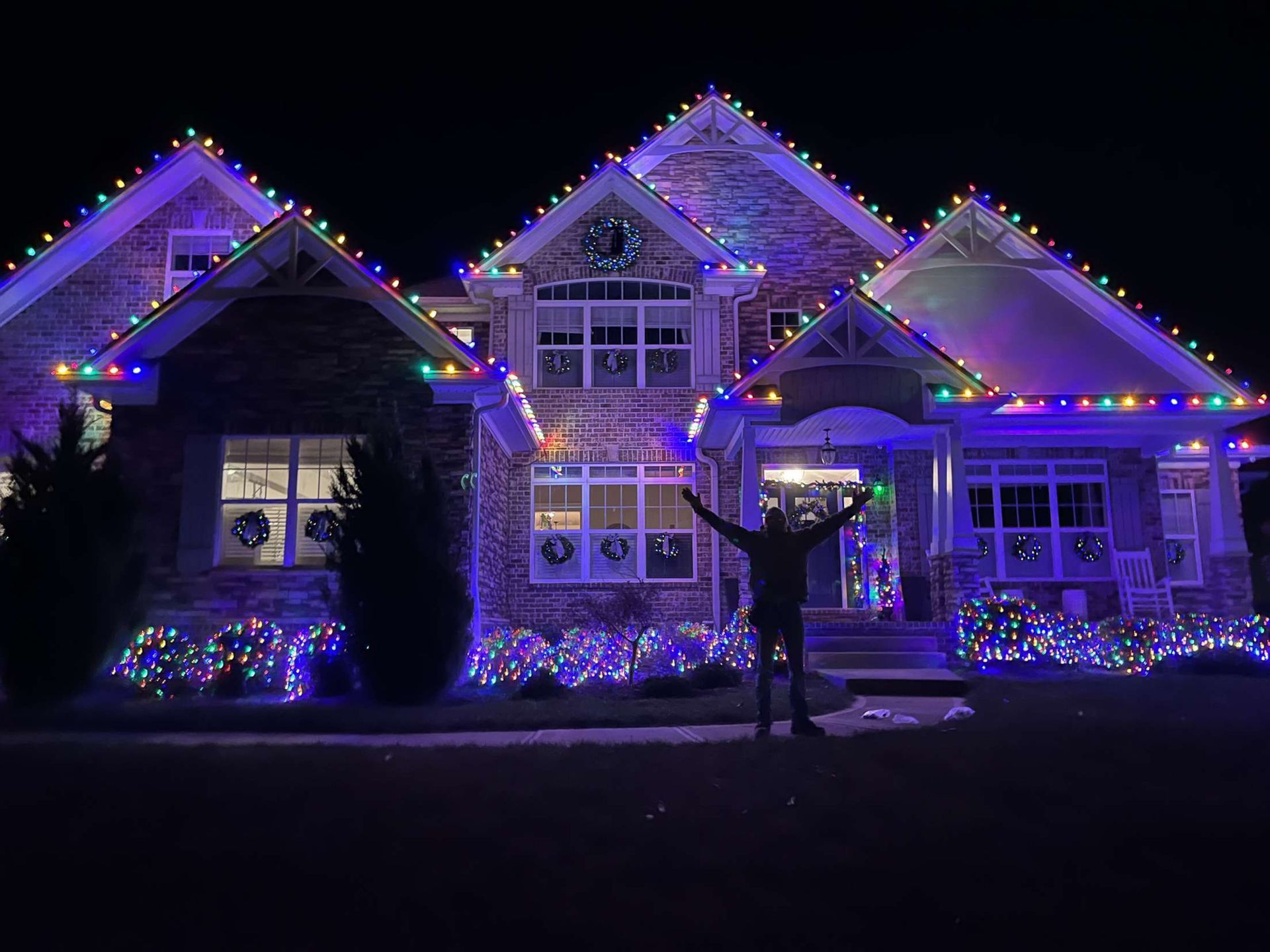 A man is standing in front of a house decorated with christmas lights.