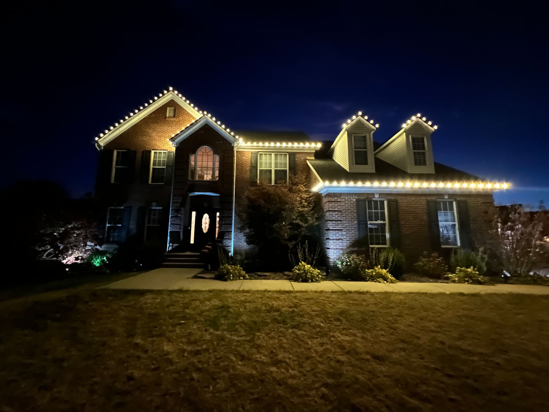 A large brick house is lit up with christmas lights at night.