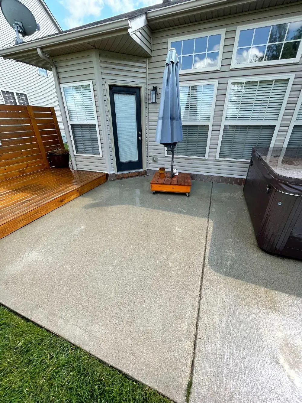 A patio with an umbrella and a hot tub in front of a house.
