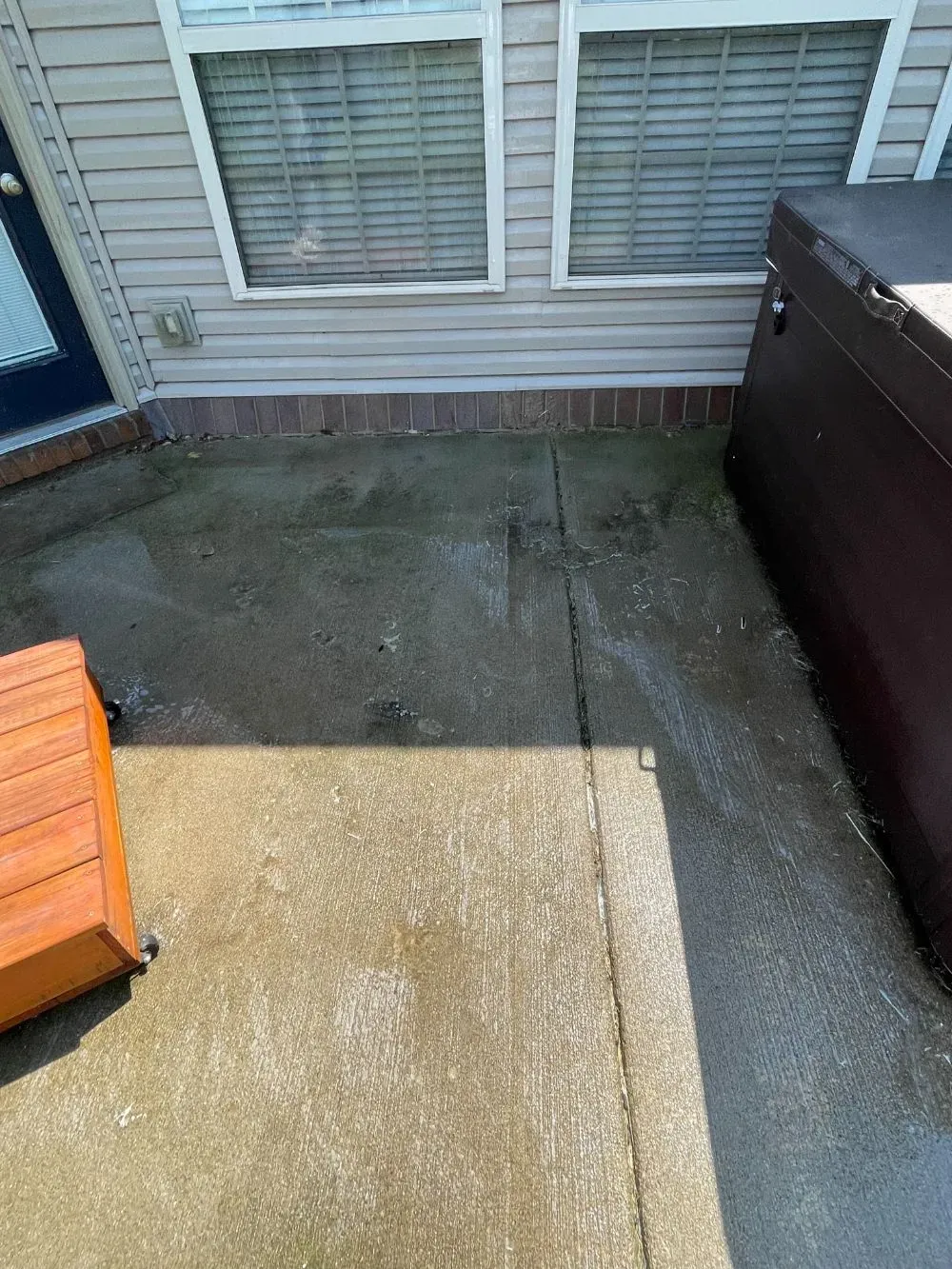 A concrete patio with a wooden bench in front of a house.