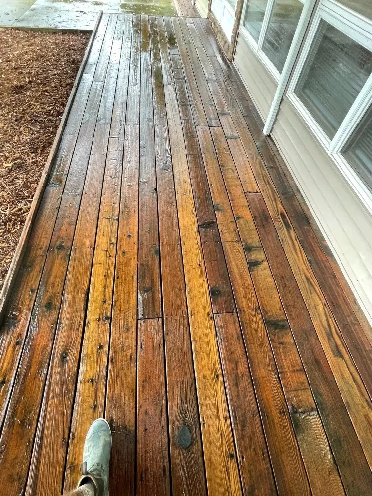 A person is standing on a wooden deck next to a house.