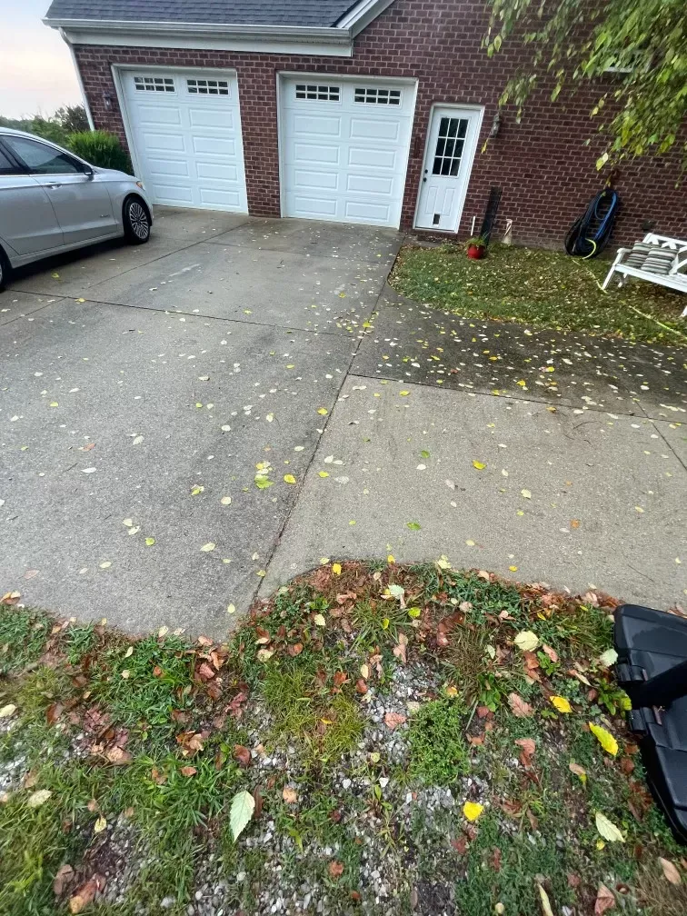 A car is parked in front of a brick house with two garage doors.