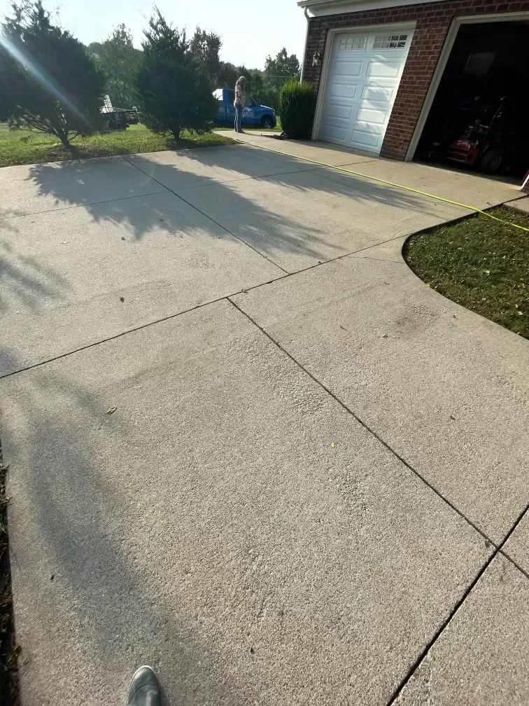A person is standing on a concrete driveway in front of a garage.