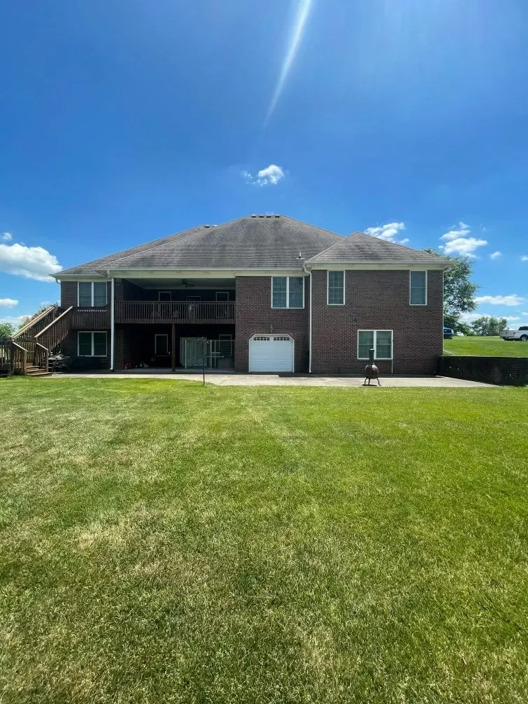 The back of a large brick house with a large lawn in front of it.