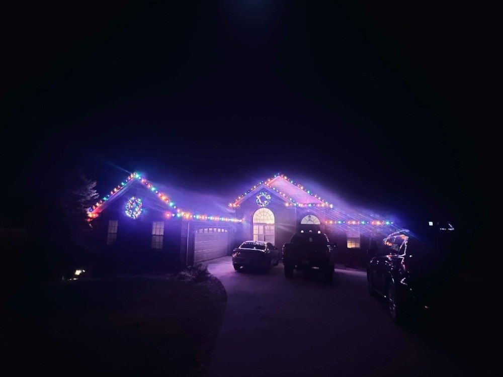 A house decorated with christmas lights at night with cars parked in front of it.