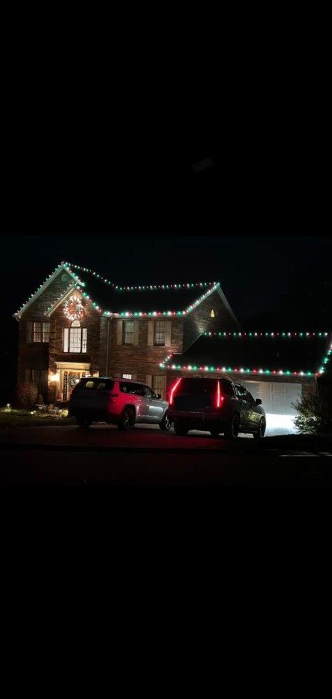A house is decorated with christmas lights and cars are parked in front of it.