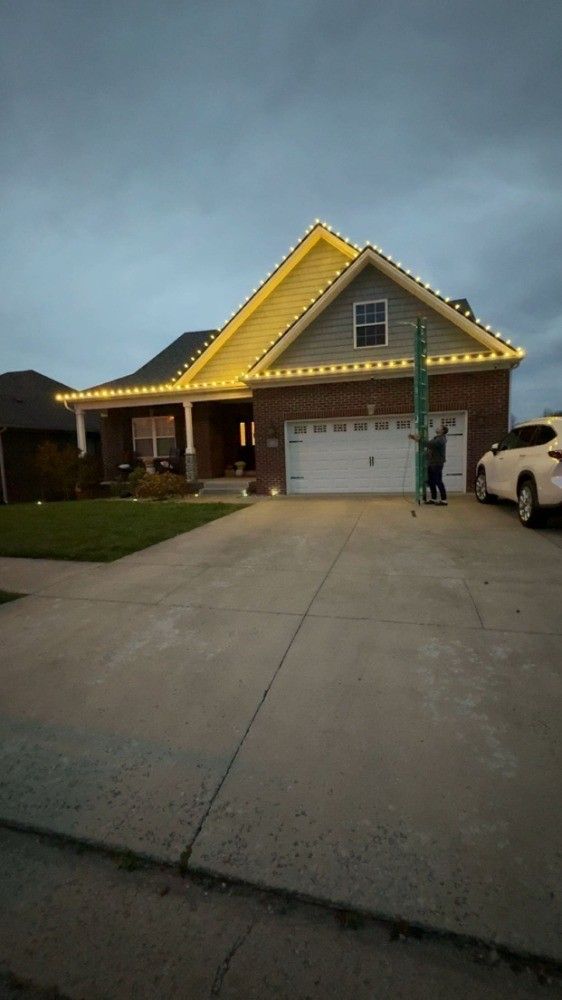 A house with christmas lights on the roof and a car parked in front of it.