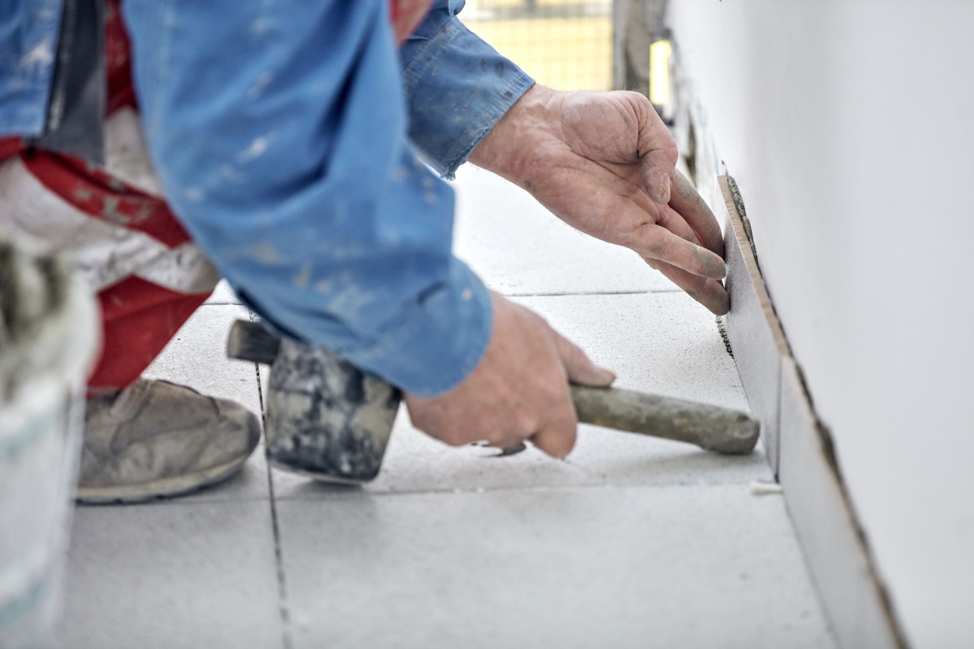 Person installing tile, using a hammer to tap a tile into place on a wall and floor. Person installing tile, using a hammer to tap a tile into place on a wall and floor.