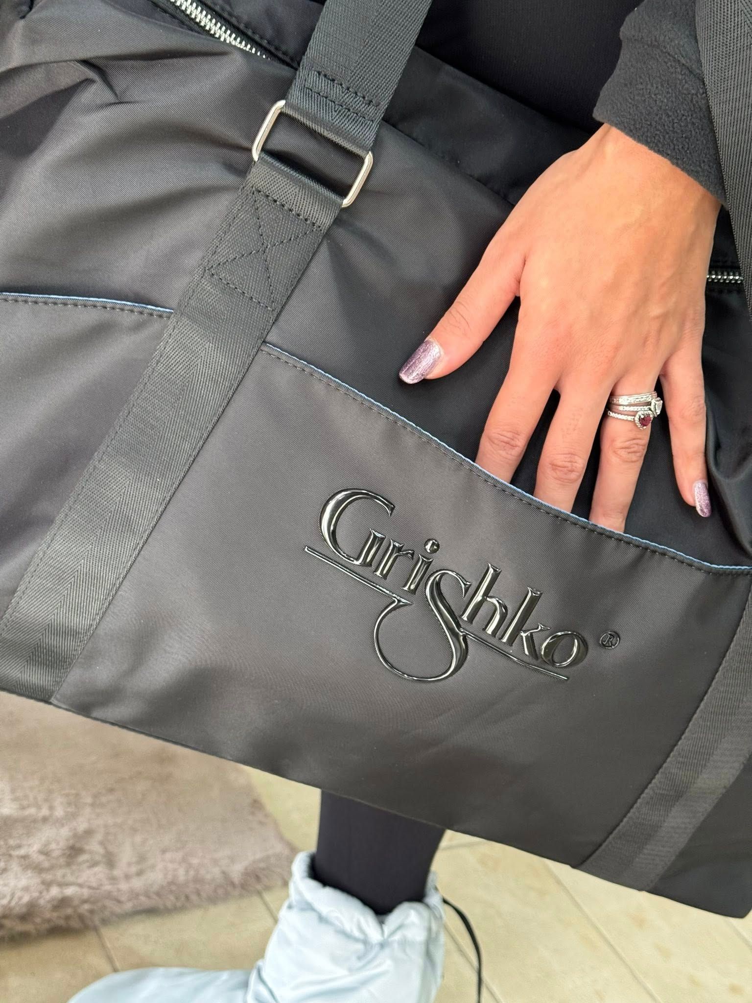 Mano di donna nella tasca di una borsa nera. La borsa ha il logo 