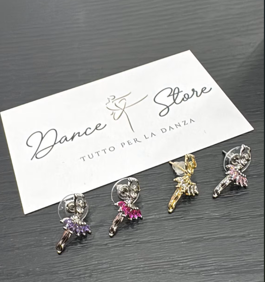Quattro orecchini a forma di ballerina con gioielli, accanto a un cartoncino bianco con il logo 