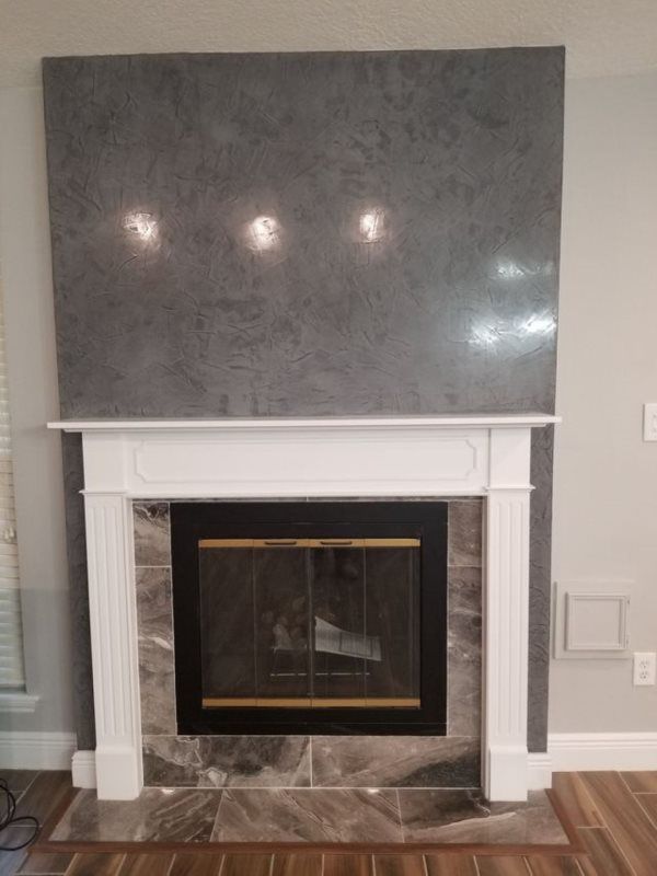 A fireplace in a living room with a gray tile wall and a white mantle.