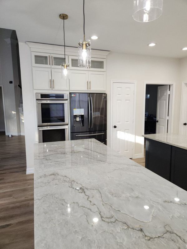 A kitchen with a marble counter top , stainless steel appliances , and white cabinets.