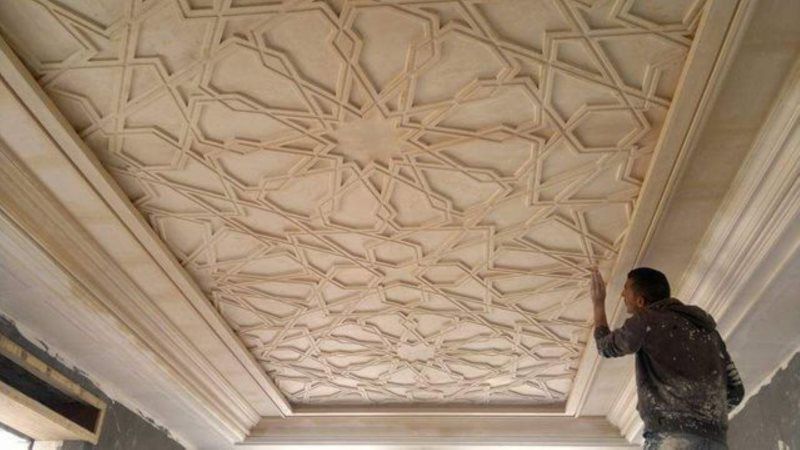 A man is painting a ceiling with a pattern on it.