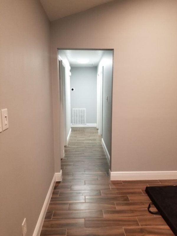 A hallway with a wooden floor and gray walls leading to a room.