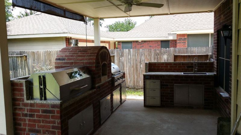 An outdoor kitchen with a brick oven and a stainless steel grill