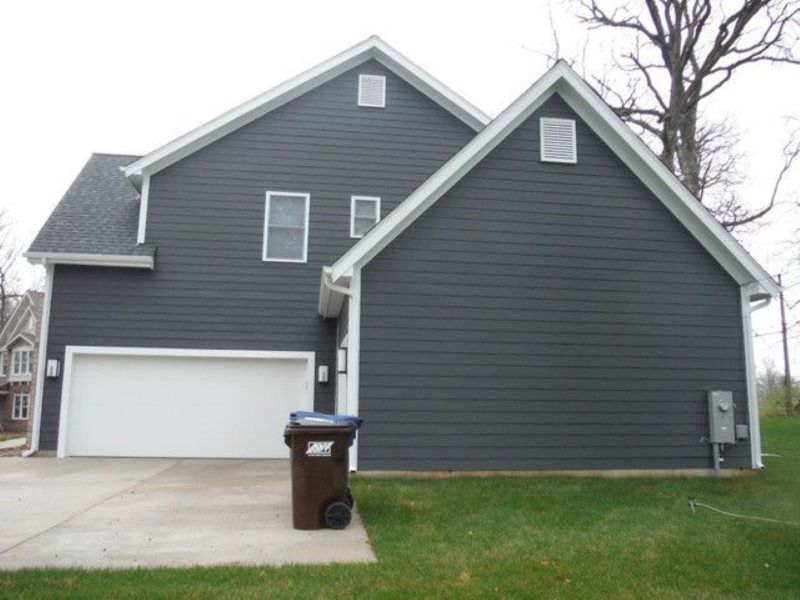 A gray house with a white garage door and a trash can in front of it