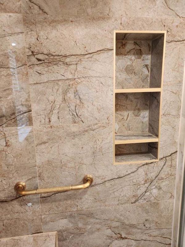 A bathroom with a marble wall and a shelf in the shower.