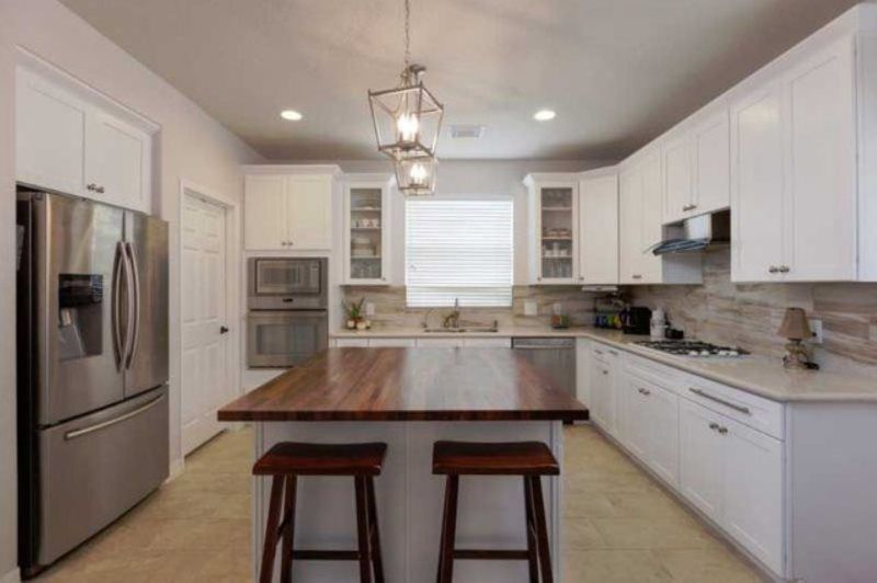 A kitchen with white cabinets , stainless steel appliances , a large island and two stools.