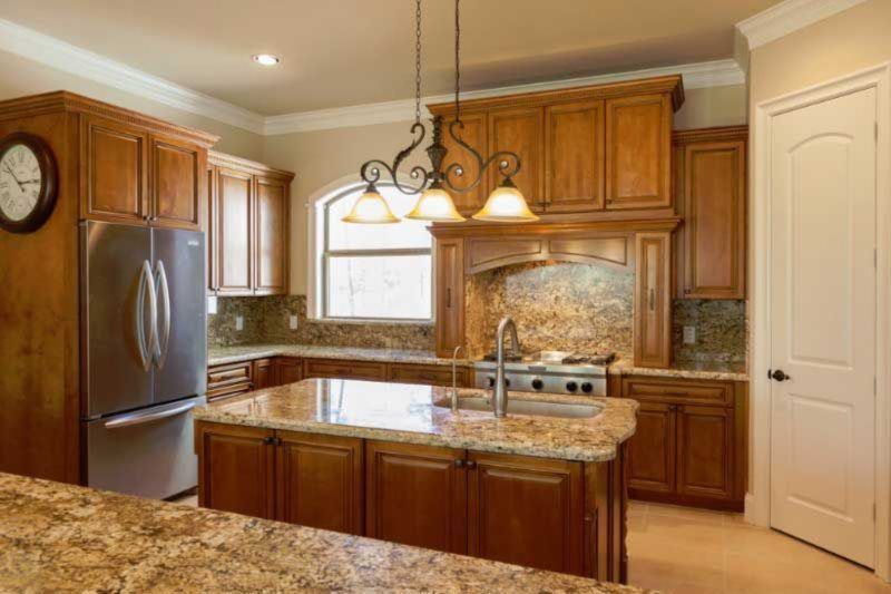 A kitchen with wooden cabinets , granite counter tops , a refrigerator and a sink.