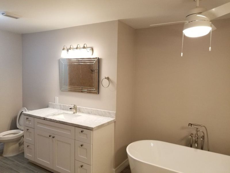 A bathroom with a tub , sink , toilet , mirror and ceiling fan.