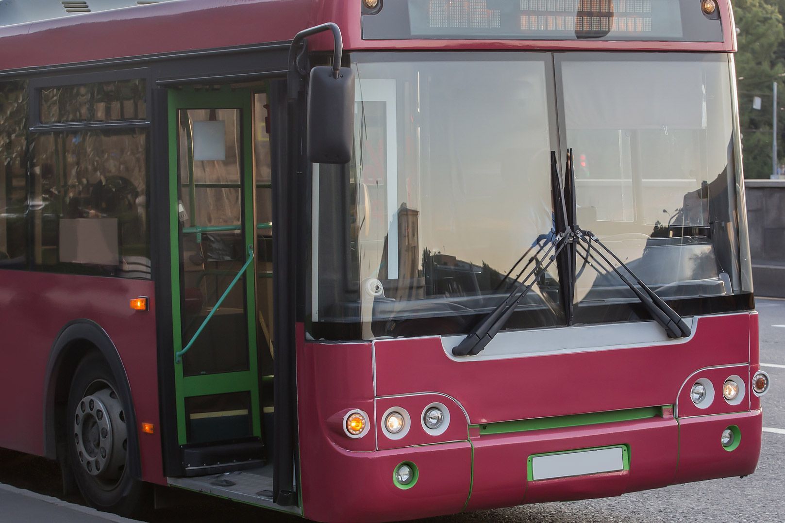 Red bus with open door, parked, with windshield wipers and headlights.