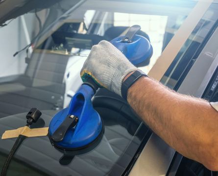 Person with a safety glove using a blue suction cup to lift or manipulate a car windshield.