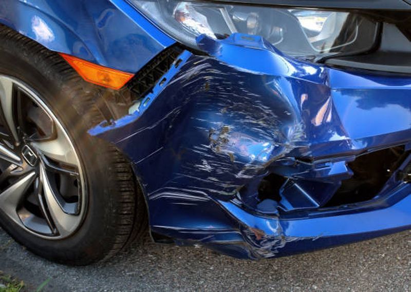 Damaged blue car front end with significant dents and scratches.