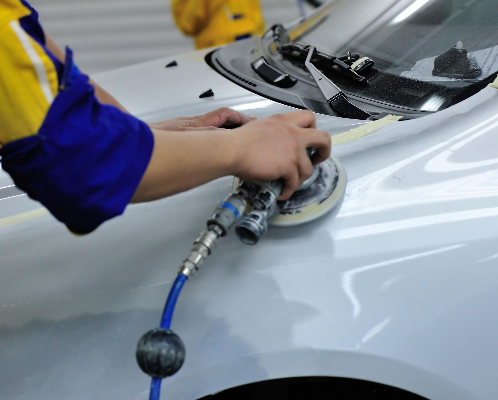 Person using a sander on a car's painted surface in a garage.