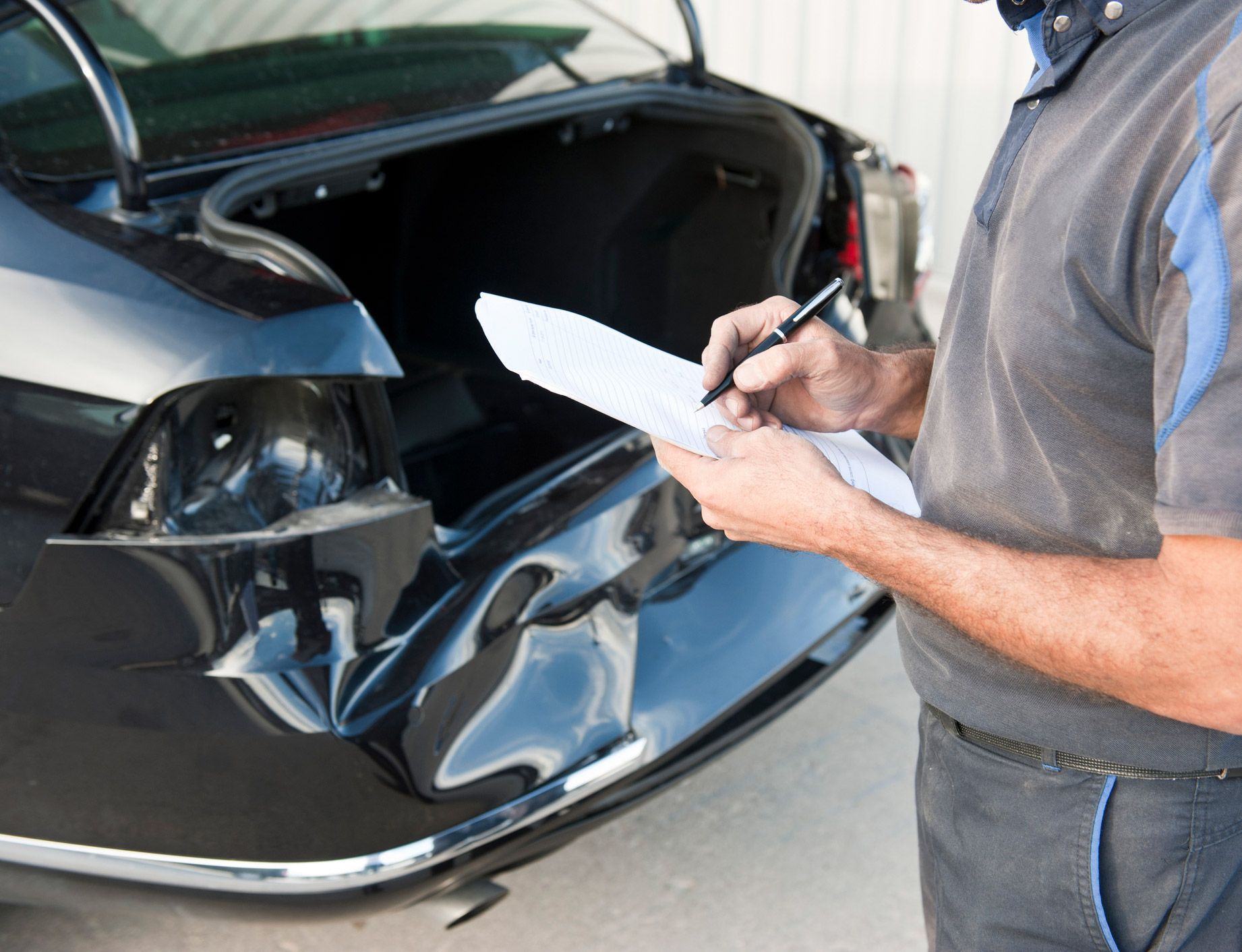 Mechanic assessing damage to a black car's rear bumper. Trunk open.
