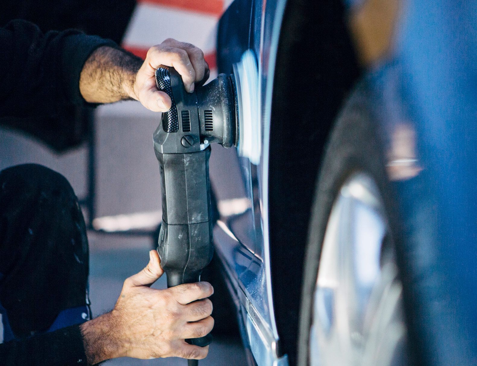 Person polishing a blue car with a handheld electric polisher.