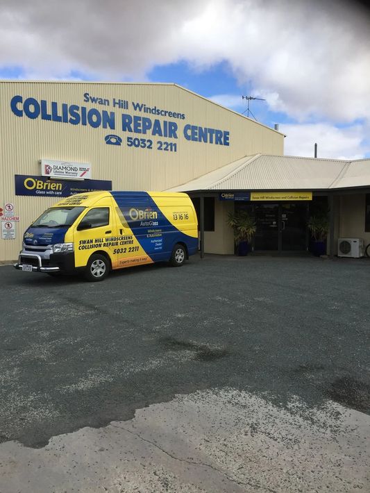 Yellow and blue van parked outside Swan Hill Collision Repair Centre. Building with blue sign and gravel ground.