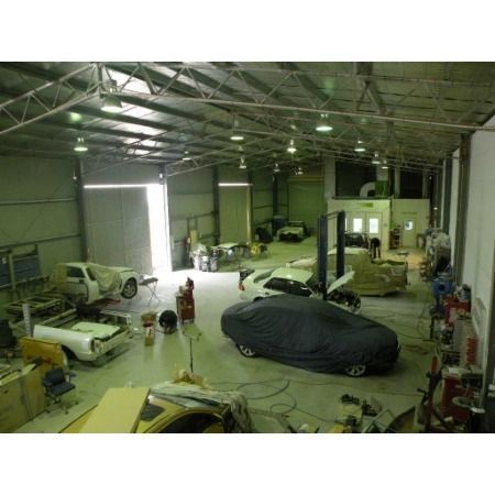Large auto body shop with several cars in various states of repair; a covered car sits center.