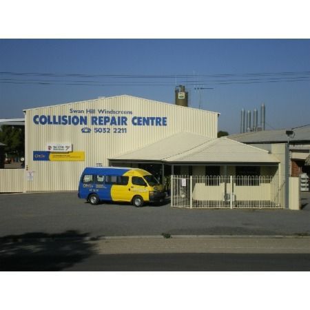 Collision repair center, large white building with blue sign, yellow and blue van parked outside.