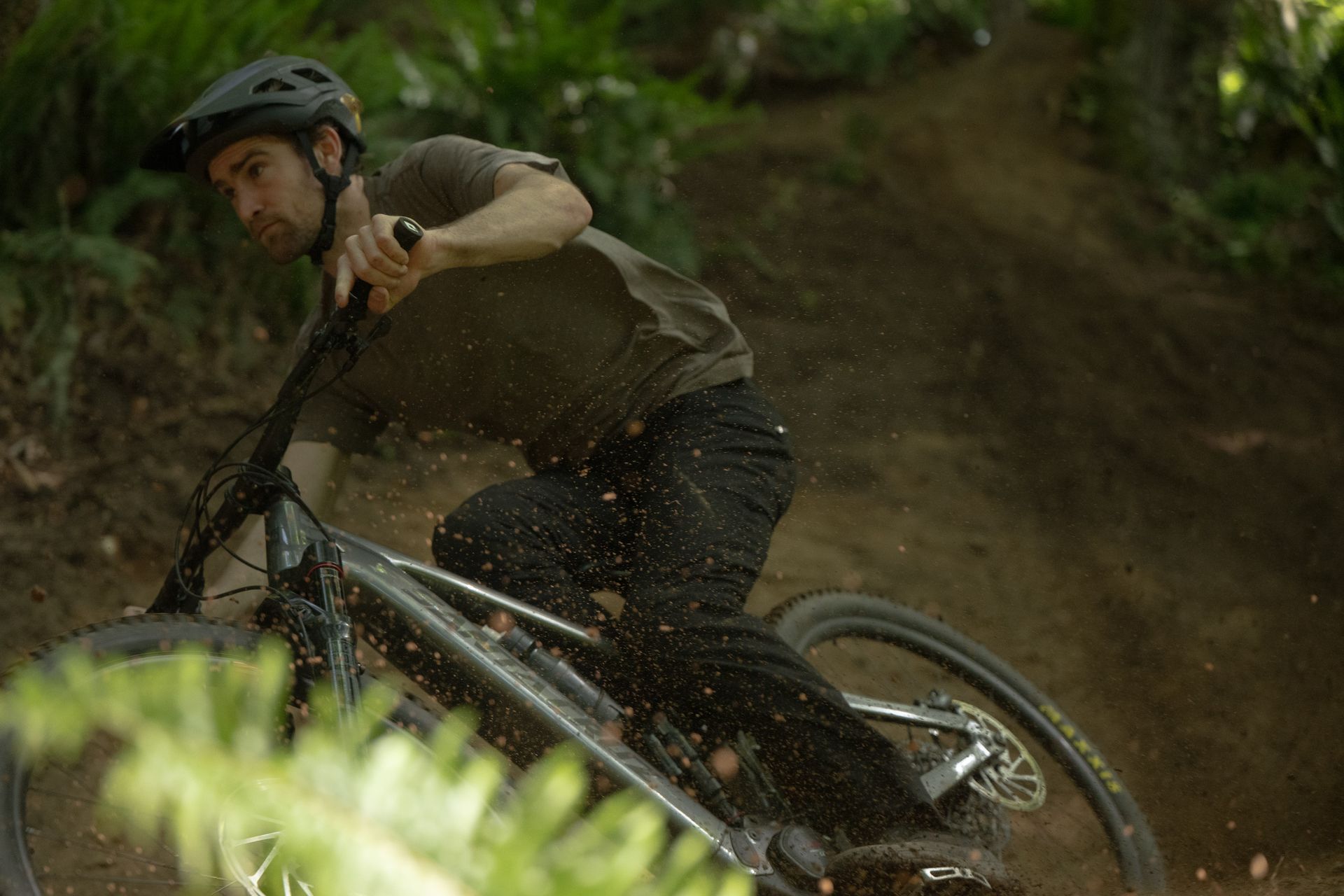 Cyclist in a helmet and sunglasses adjusting them outdoors, wearing a teal cycling jersey.