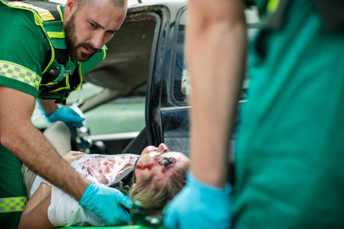 Paramedics tending to a woman injured in a car accident. She has facial injuries and is on a stretcher.