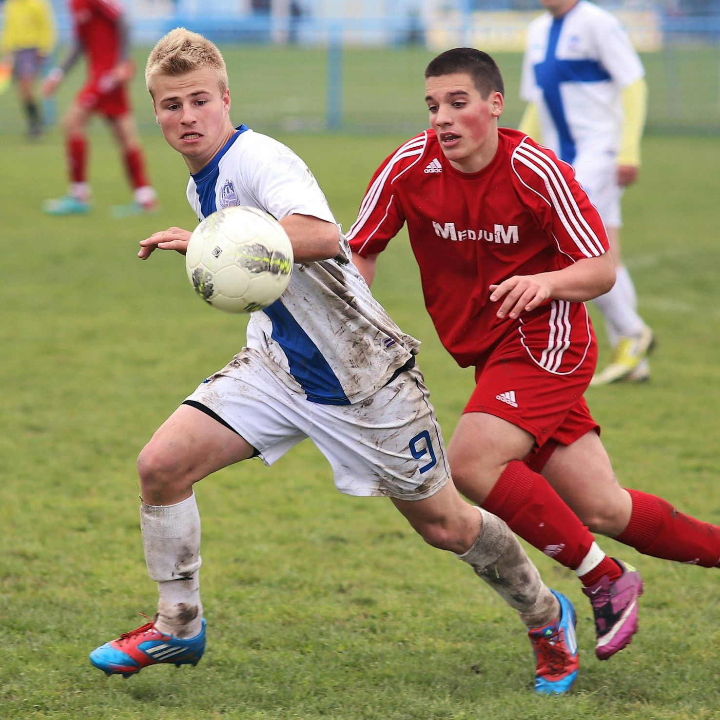 Soccer players in action: white-clad player dribbles the ball, red-clad player attempts to tackle.