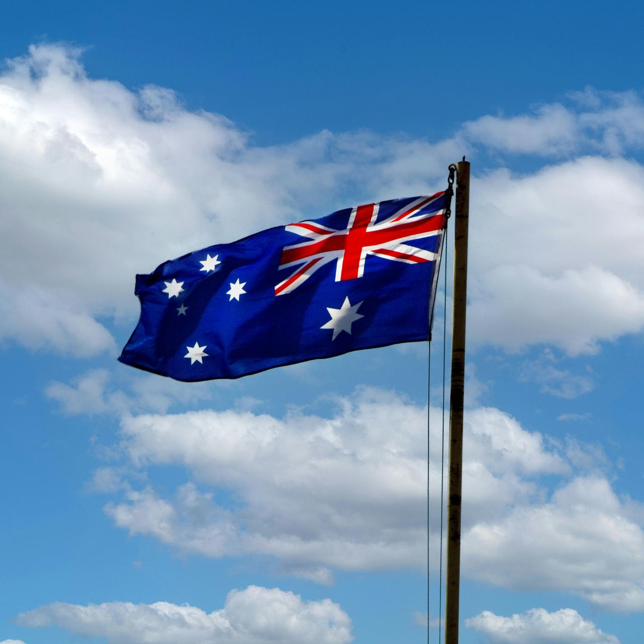 Australian flag waving in the wind against a blue sky with fluffy white clouds.