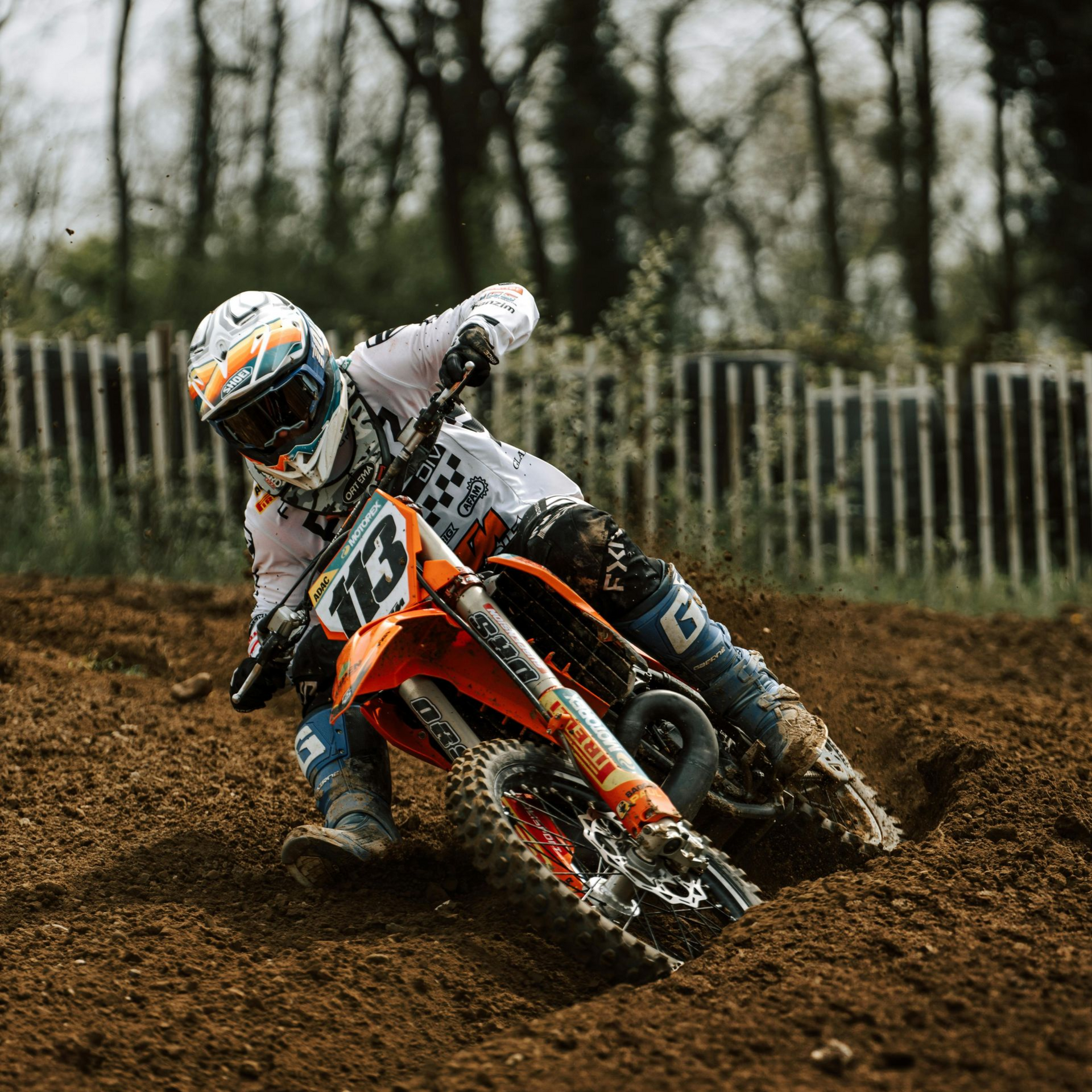 Motocross racer on an orange bike, leaning into a turn on a dirt track.