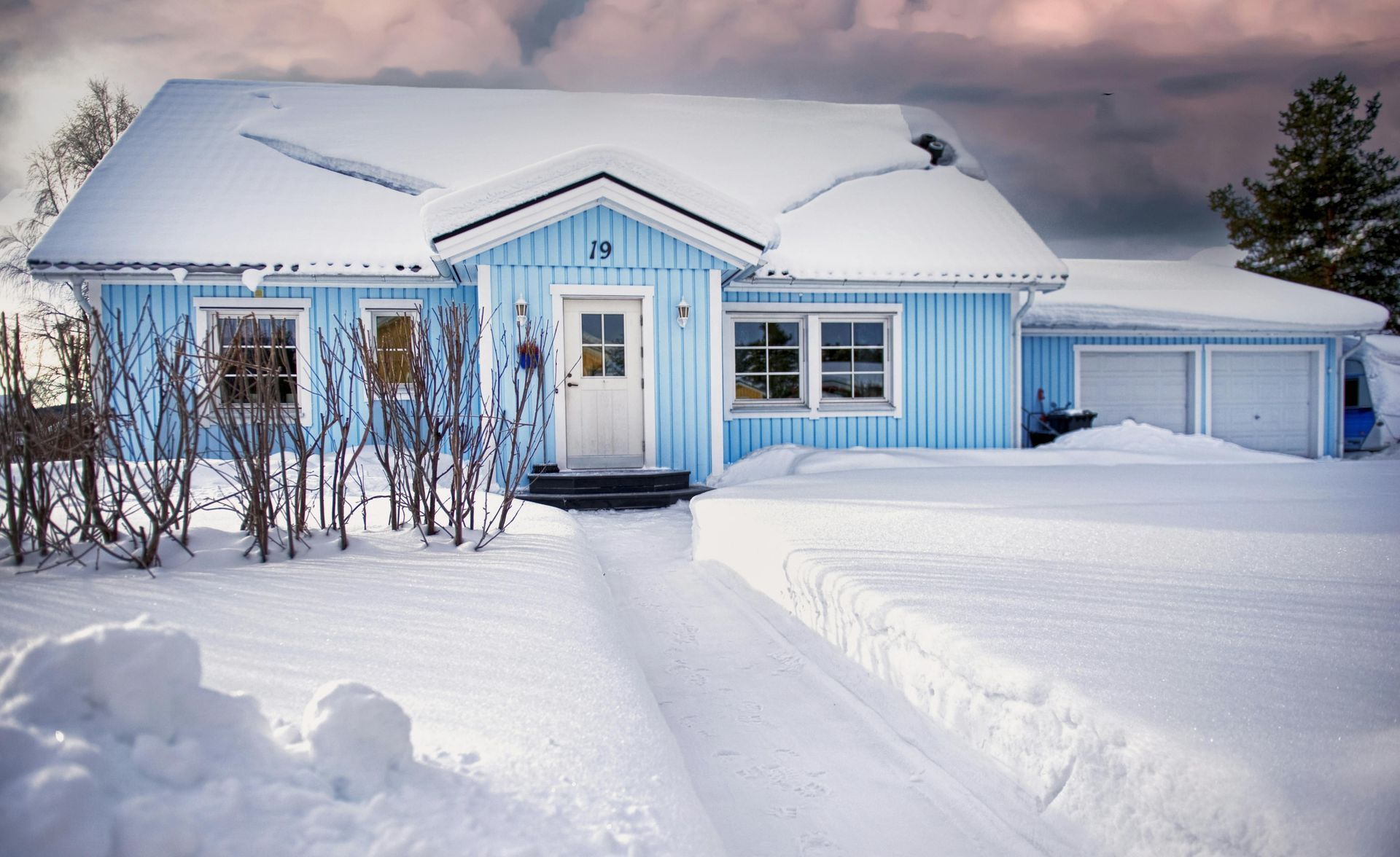 A bright blue house with white trim covered in deep snow, featuring a cleared path leading to the front door.