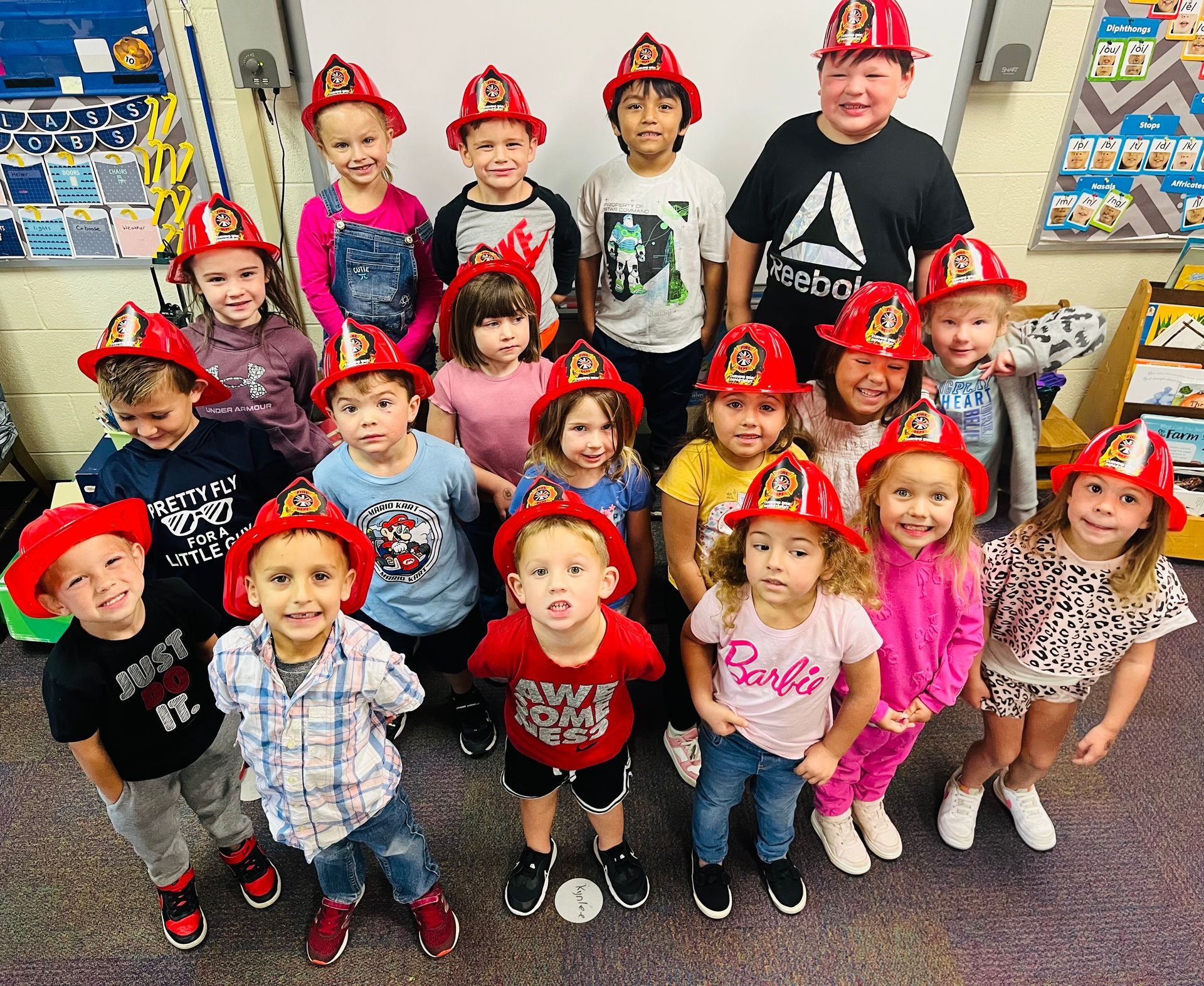 A group of children wearing firefighter hats are posing for a picture in a classroom.