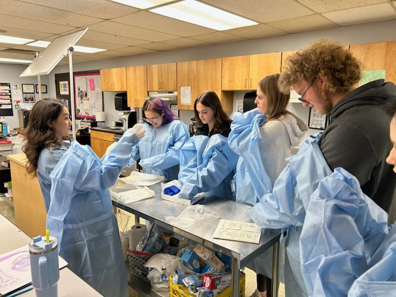 A group of students are standing around a table in a classroom lab.