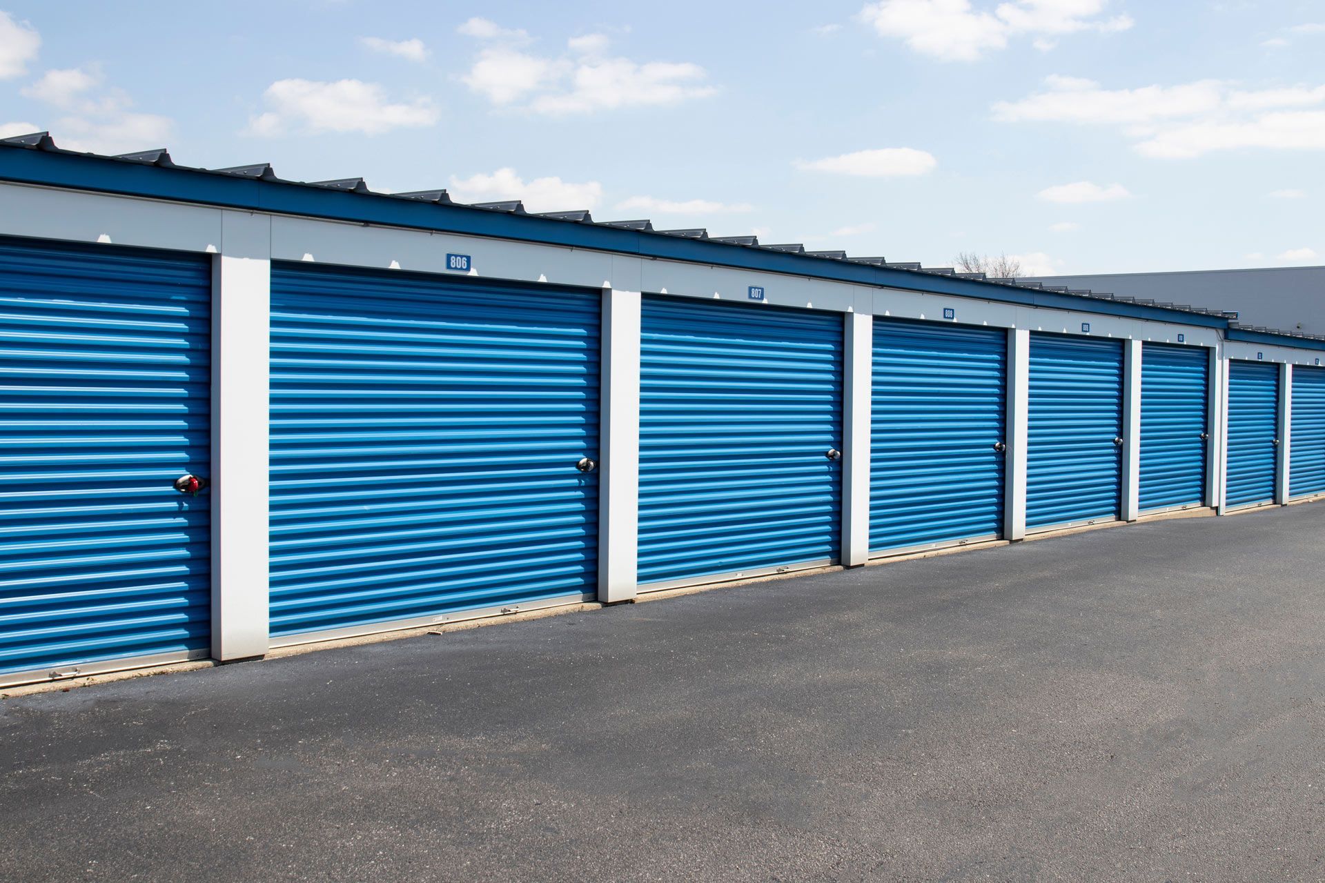 Rows of blue roll-up storage unit doors along a paved facility under a partly cloudy sky. Rows of blue roll-up storage unit doors along a paved facility under a partly cloudy sky.