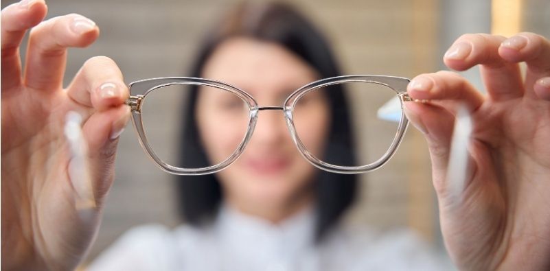 A brunette woman holds a pair of transparent glasses in her hands